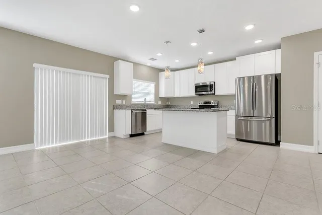 a kitchen with stainless steel appliances granite countertop a refrigerator a sink a stove and white cabinets