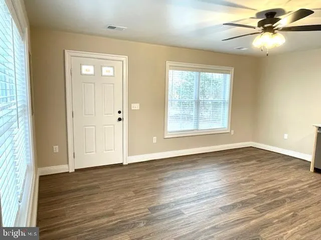 an empty room with wooden floor fan and windows