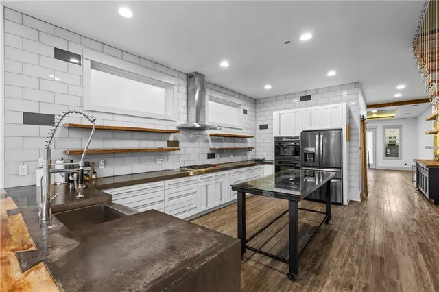 a kitchen with stainless steel appliances a refrigerator a sink a stove top oven a dining table and chairs with wooden floor