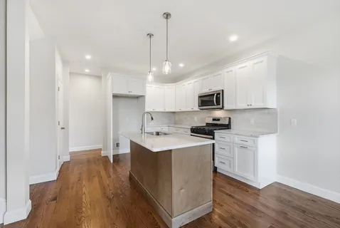 a kitchen with stainless steel appliances kitchen island a white cabinets and a wooden floor