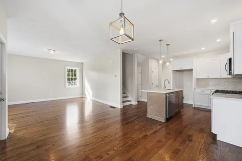 a view of an empty room and kitchen with wooden floor