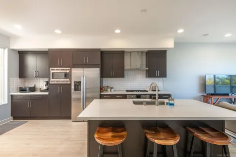 a kitchen with stainless steel appliances a sink a stove a refrigerator cabinets and chairs