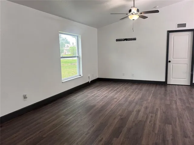 an empty room with wooden floor chandelier fan and windows