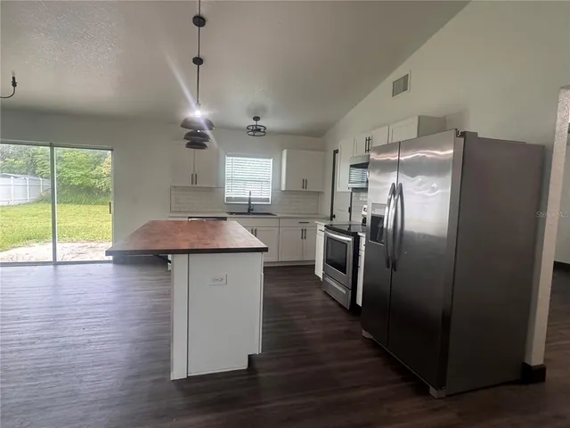 a kitchen with stainless steel appliances a refrigerator a sink dishwasher a stove and white cabinets with wooden floor