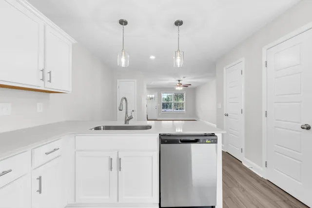 a kitchen with a sink dishwasher and white cabinets with wooden floor