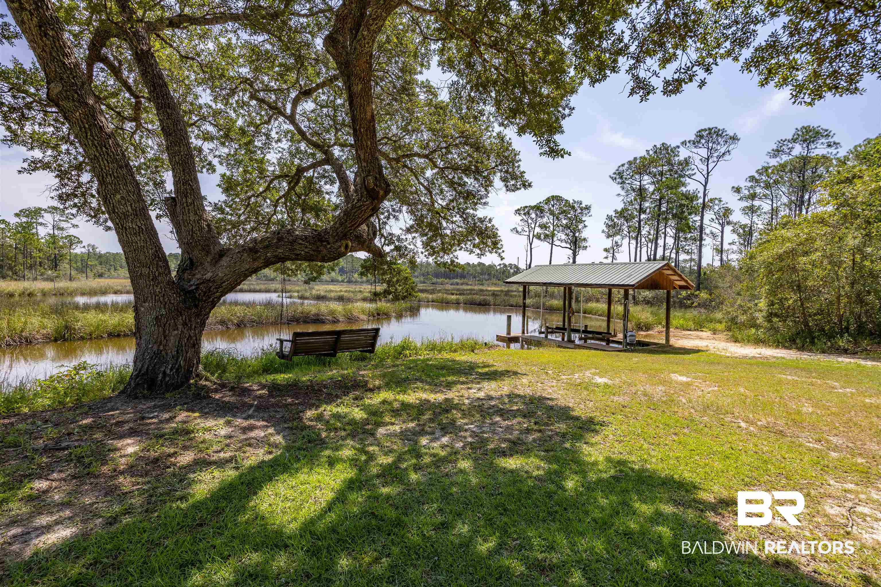 13677 Rebel Road Coden, AL 36523 - Photo 51 of 61 Waterfront property featuring a covered boat dock with a metal roof, a natural water setting, mature trees, and a wooden bench