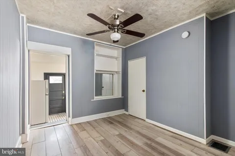 a view of an empty room with wooden floor and a ceiling fan