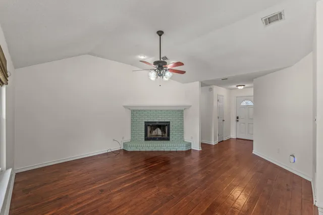 a view of an empty room with wooden floor fireplace and a window