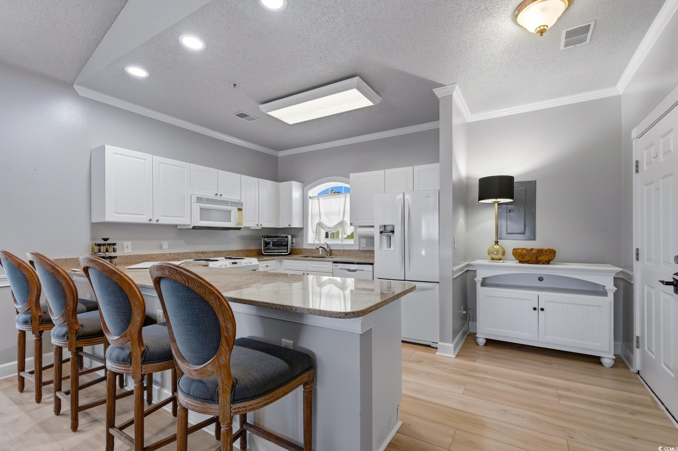 4839 Carnation Circle, Unit 305 Myrtle Beach, SC 29577 - Photo 2 of 24 Kitchen featuring a textured ceiling, white appliances, light stone countertops, white cabinetry, and a kitchen bar