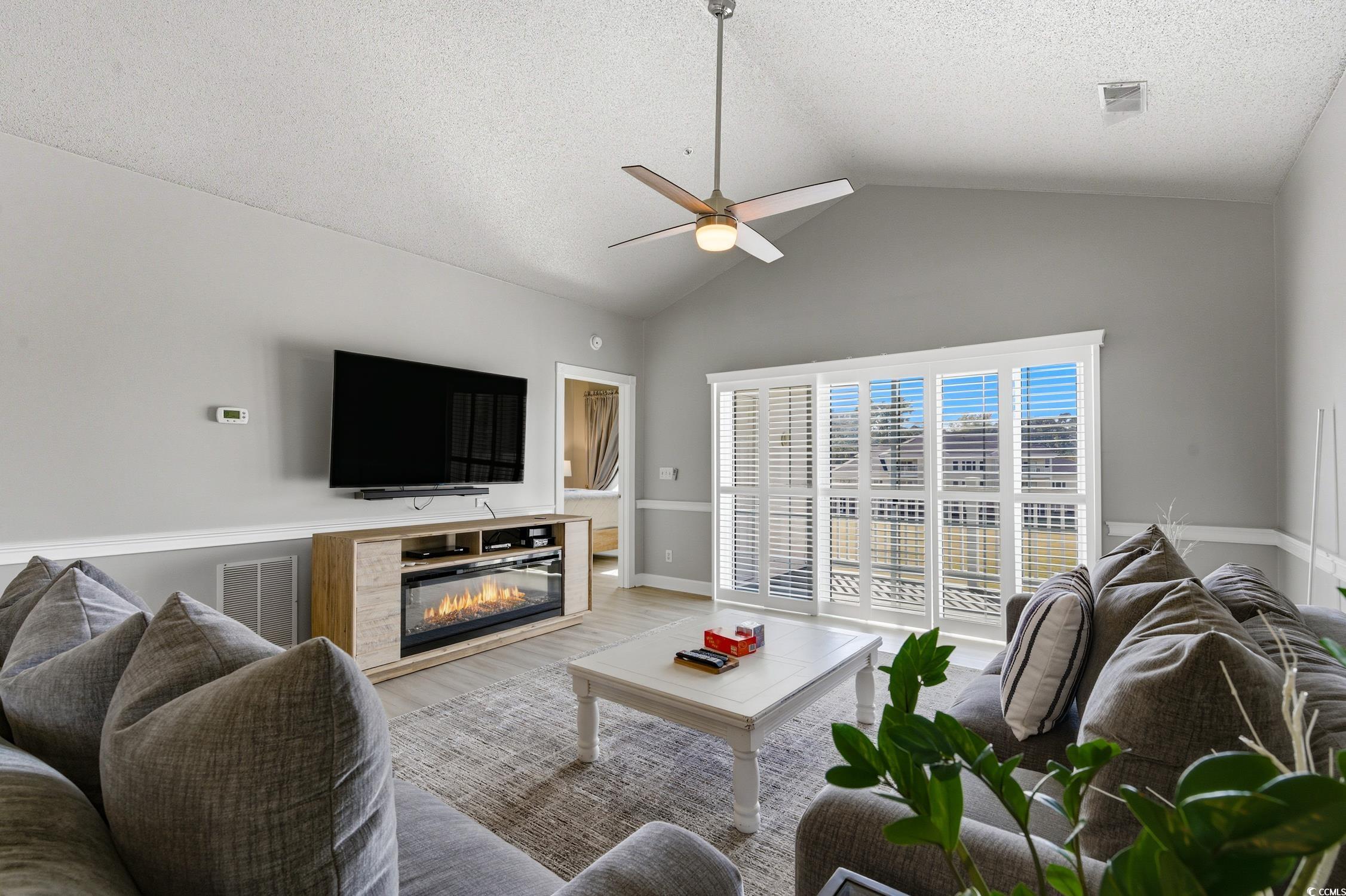 4839 Carnation Circle, Unit 305 Myrtle Beach, SC 29577 - Photo 8 of 24 Living area with a glass covered fireplace, wood finished floors, a ceiling fan, a textured ceiling, and high vaulted ceiling