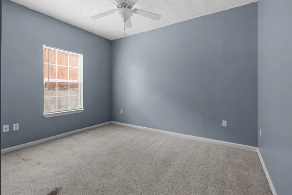 an empty room with a chandelier fan and windows