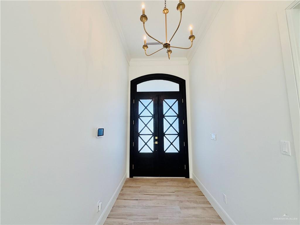 807 Ramirez Street Mission, TX 78573 - Photo 3 of 16 Elegant foyer showcasing a striking black double-door entry with arched transom and cross-panel glazing, wood tile flooring, and a brass multi-arm pendant fixture overhead