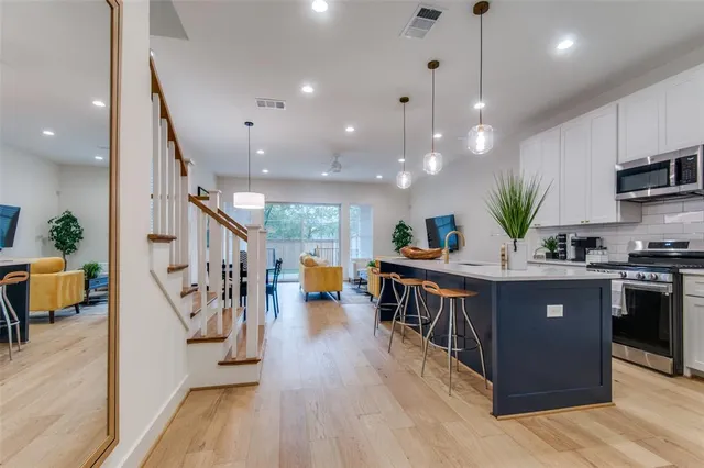 a kitchen with stainless steel appliances granite countertop a refrigerator a stove a sink dishwasher and a dining table with wooden floor