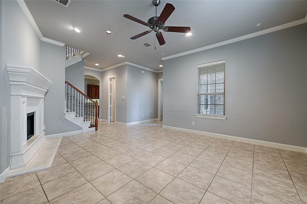 8329 Moore Street Frisco, TX 75034 - Photo 4 of 30 Unfurnished living room featuring ornamental molding, light tile patterned floors, ceiling fan, a fireplace with raised hearth, and stairway