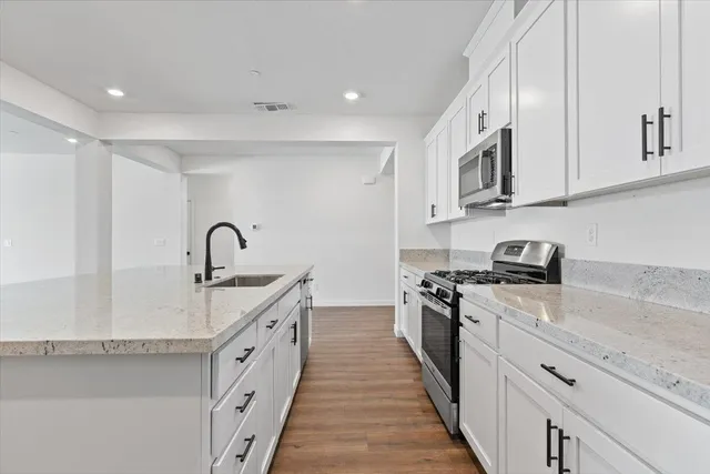 a large white kitchen with stainless steel appliances granite countertop a stove a sink a refrigerator and white cabinets