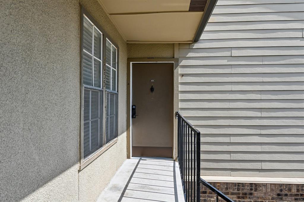 5300 Keller Springs Road, Unit 2055 Dallas, TX 75248 - Photo 23 of 24 Entryway featuring a solid door with hardware, stucco siding, horizontal plank siding, brick detailing at the base, and a black metal handrail