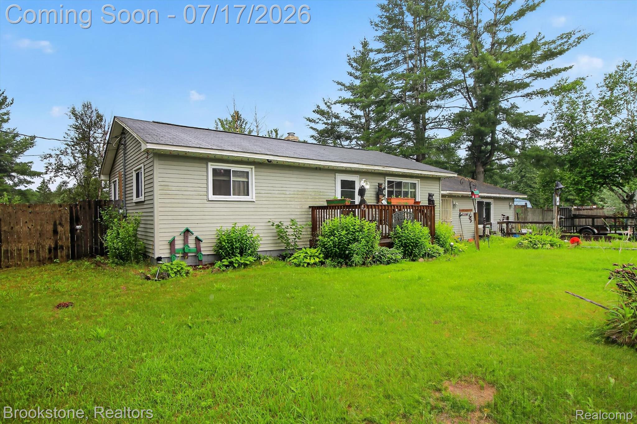 22709 Pleasant Valley Road Hillman, MI 49746 - Photo 2 of 42 Expansive green lawn surrounds a property featuring light-colored siding, a dark-pitched roof, and a wooden deck