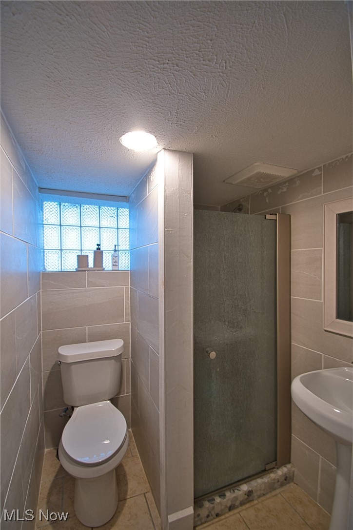 5402 Biddulph Road Cleveland, OH 44144 - Photo 15 of 20 Bathroom featuring tile patterned floors, toilet, a textured ceiling, tile walls, and a shower with shower door