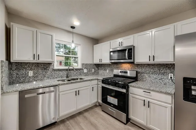 a kitchen with granite countertop white cabinets stainless steel appliances and a sink