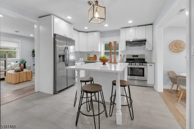 a kitchen with stainless steel appliances a refrigerator a stove a sink a dining table and chairs with wooden floor