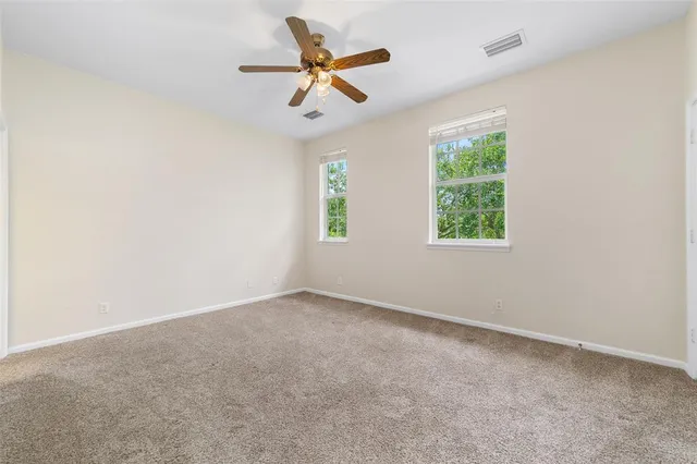 an empty room with ceiling fan and windows