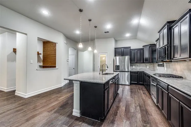a kitchen with stainless steel appliances kitchen island granite countertop a stove a sink dishwasher a refrigerator and a oven with wooden floor