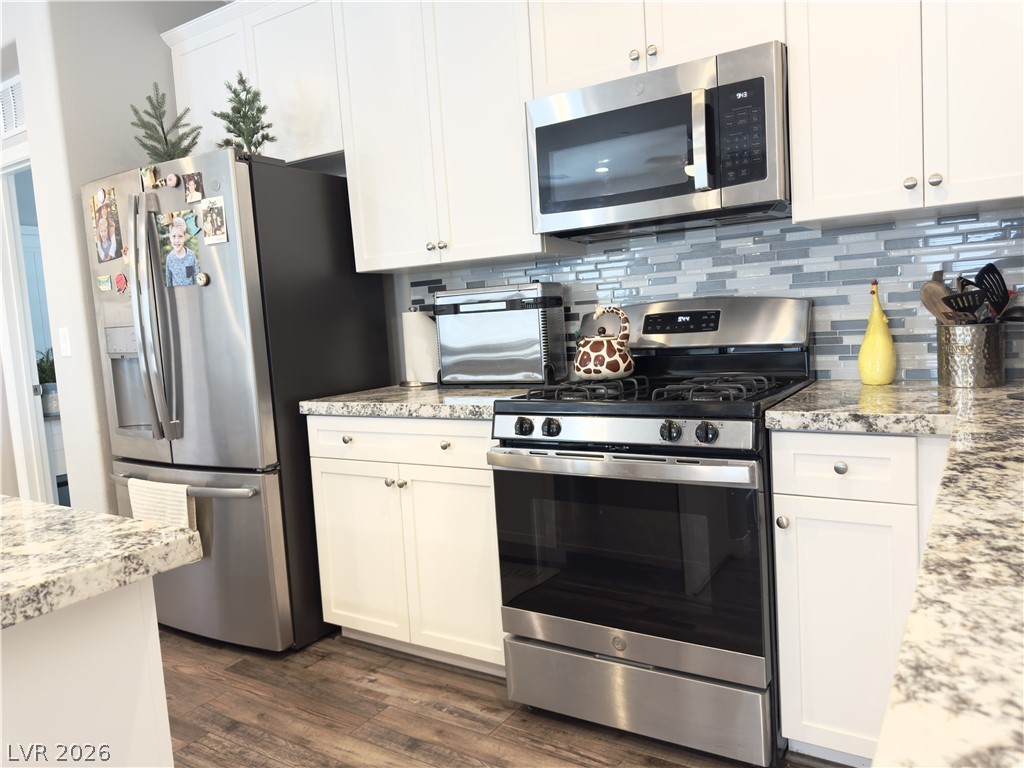 78 Summer Rhapsody Avenue Henderson, NV 89015 - Photo 4 of 31 Kitchen featuring stainless steel appliances, light stone counters, white cabinets, dark wood-type flooring, and decorative backsplash