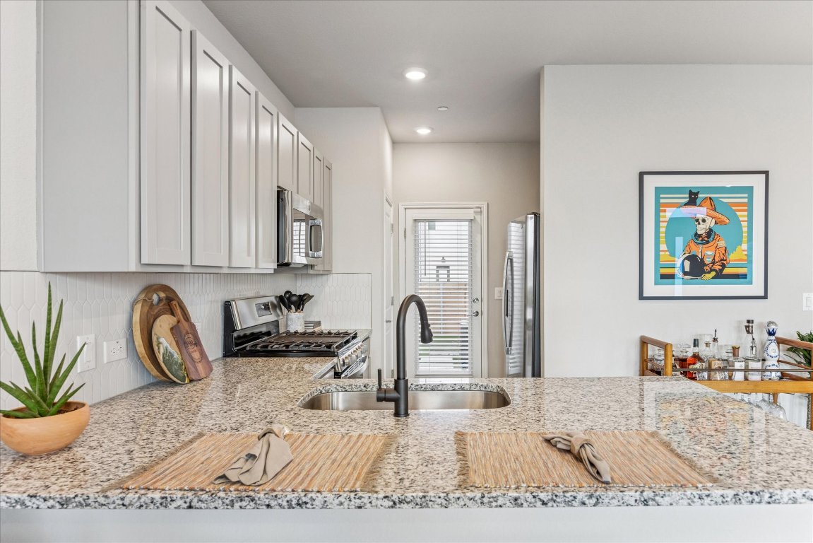 9015 Cattle Baron Path, Unit 1002 Austin, TX 78747 - Photo 5 of 21 a kitchen with stainless steel appliances granite countertop a sink a stove a dining table and chairs with wooden floor