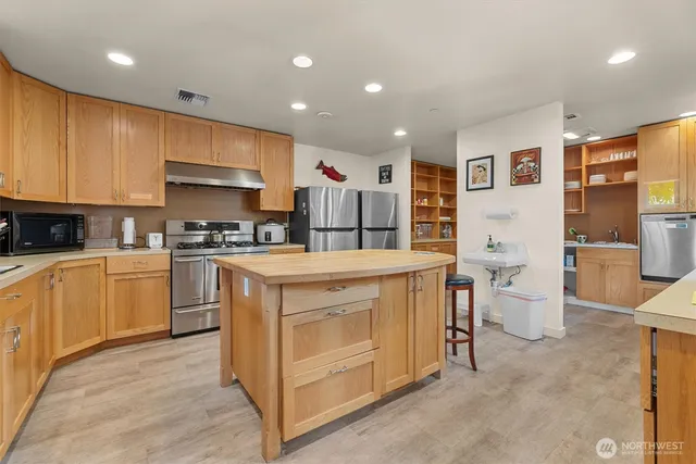 a kitchen with stainless steel appliances granite countertop wooden cabinets a sink a stove a dining table and chairs