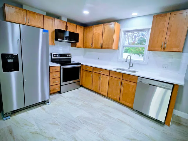 a kitchen with stainless steel appliances a stove a sink a refrigerator a sink a window and wooden floor