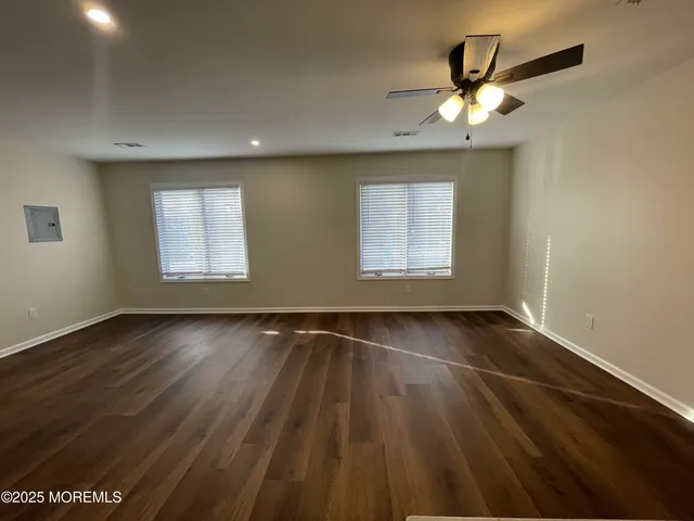 an empty room with wooden floor chandelier fan and windows