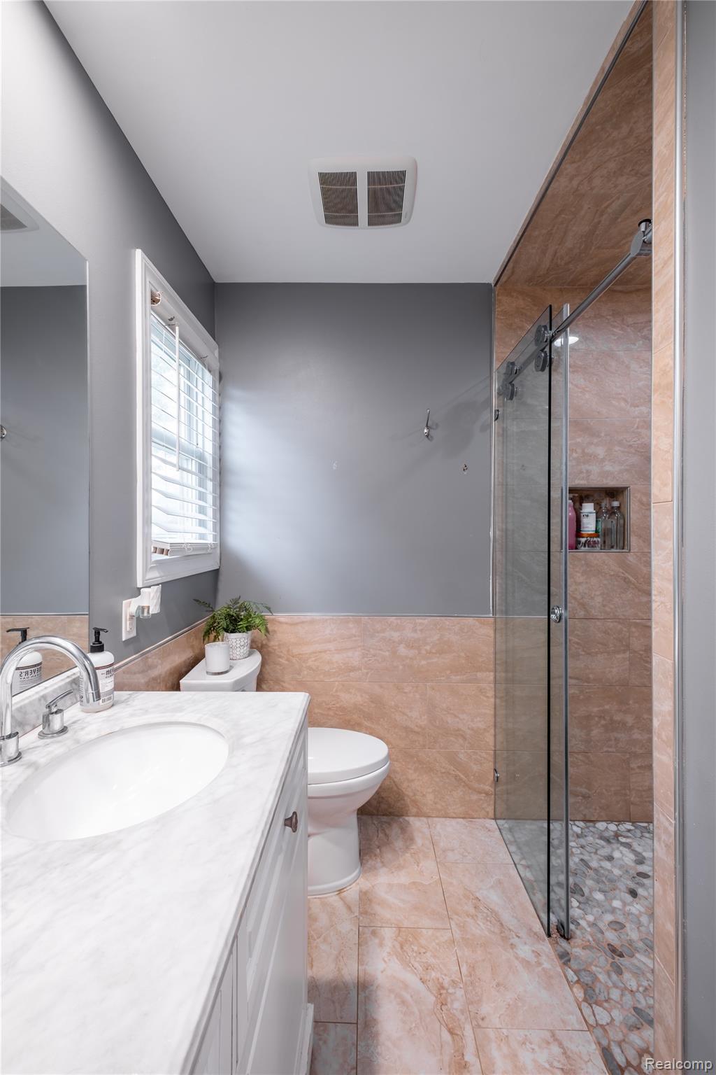 10250 Duffield Road Gaines, MI 48436 - Photo 18 of 28 Walk-in shower with a glass enclosure and pebble floor, complemented by floor-to-ceiling tile