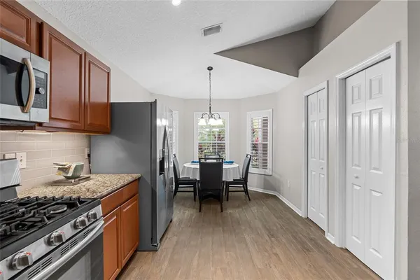a kitchen with stainless steel appliances granite countertop a stove top oven a refrigerator a dining table and chairs with wooden floor