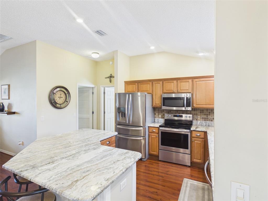 2297 Welcome Way The Villages, FL 32162 - Photo 15 of 36 a kitchen with stainless steel appliances granite countertop a refrigerator a stove and a sink with wooden floor