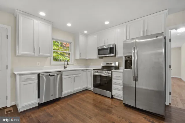 a kitchen with granite countertop stainless steel appliances a refrigerator cabinets and wooden floor