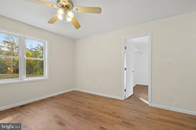 an empty room with wooden floor chandelier fan and windows