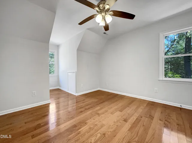 an empty room with wooden floor chandelier fan and windows