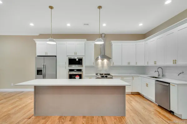 a large kitchen with kitchen island a sink a stove a refrigerator and white cabinets with wooden floor
