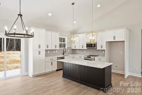 a kitchen with stainless steel appliances granite countertop a refrigerator a sink dishwasher a stove and white cabinets with wooden floor