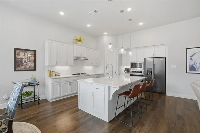 a large kitchen with stainless steel appliances a lot of white cabinets and wooden floors