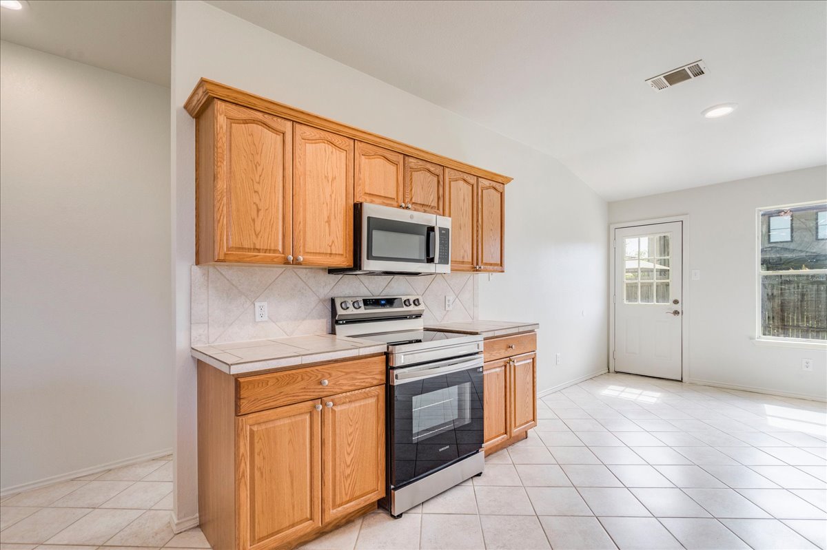 100 Easy Street Hutto, TX 78634 - Photo 8 of 36 A compact kitchen boasts warm wood cabinetry and brand new sleek stainless steel appliances, ready for culinary endeavors.