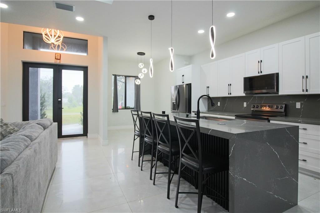 3902 4th Street Southwest Lehigh Acres, FL 33976 - Photo 9 of 34 White cabinetry, dark stone-finish countertops, and a kitchen island with pendant lighting