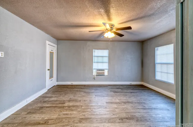 an empty room with wooden floor fan and windows
