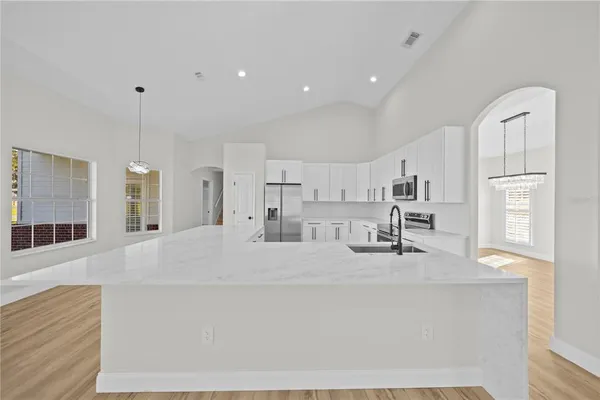 a large white kitchen with kitchen island a sink stainless steel appliances and cabinets