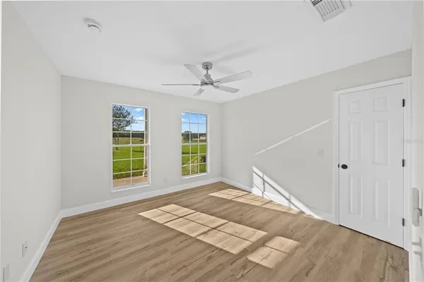 an empty room with wooden floor ceiling fan and windows