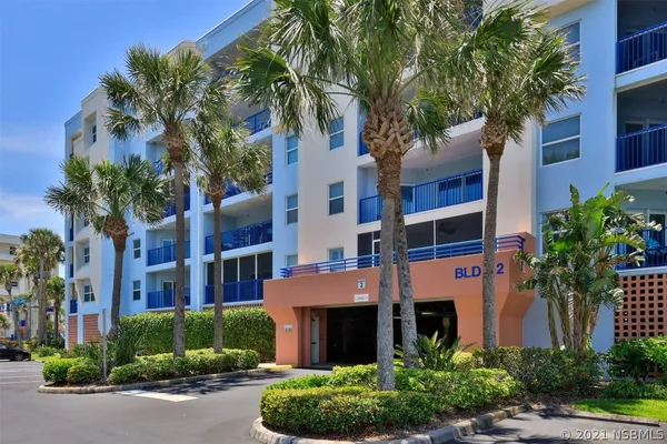 a front view of a multi story residential apartment building with yard and parking