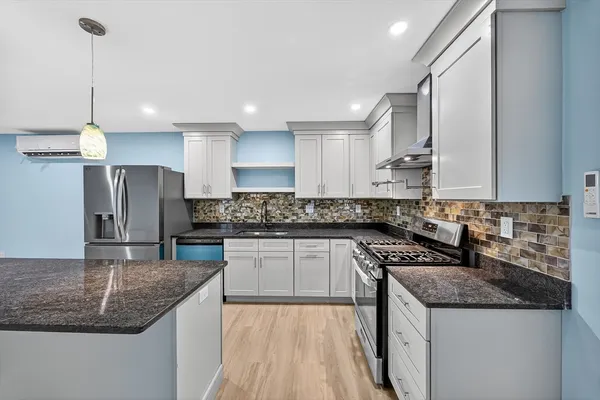 a kitchen with stainless steel appliances granite countertop a sink a stove a refrigerator and island with wooden floor