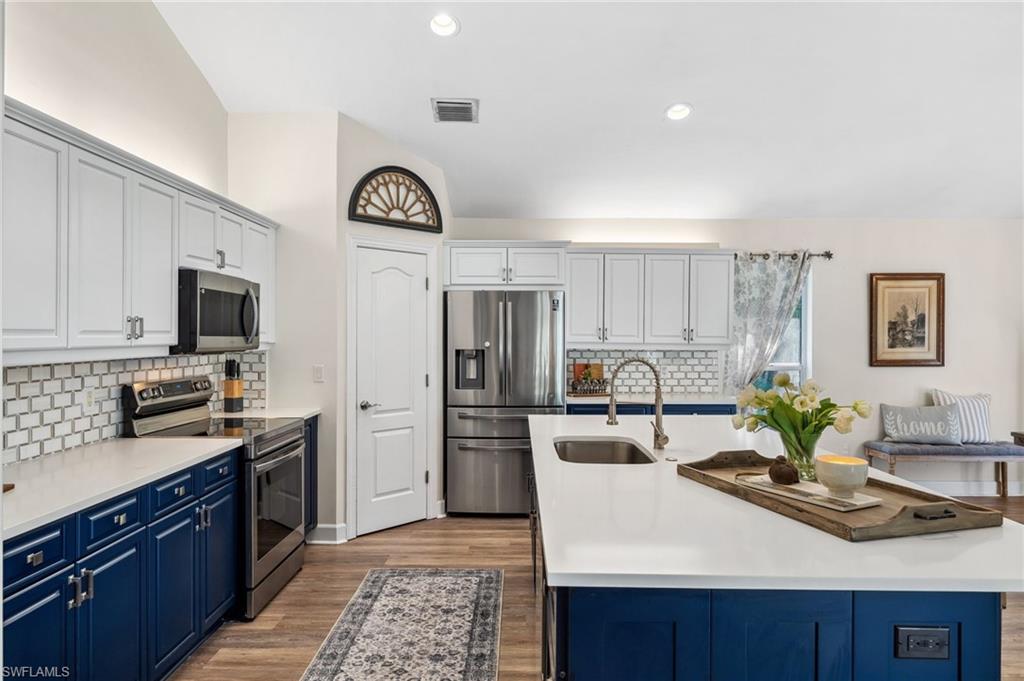 6857 Mill Run Road Naples, FL 34109 - Photo 6 of 49 Kitchen featuring blue cabinetry, visible vents, appliances with stainless steel finishes, a sink, and wood finished floors