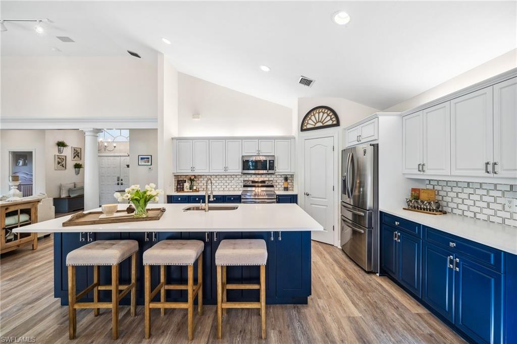 6857 Mill Run Road Naples, FL 34109 - Photo 8 of 49 Kitchen featuring decorative columns, stainless steel appliances, a sink, blue cabinets, and a kitchen bar