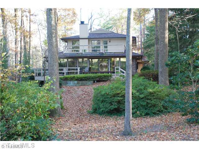 Exterior Back. Back of house with windows overlooking wooded acreage and 5th Green of Sedgefield Country Club. Deck wraps around the house off den, dining room and living room on main level and romatnic balcony off Master Bedroom. Private serenity!